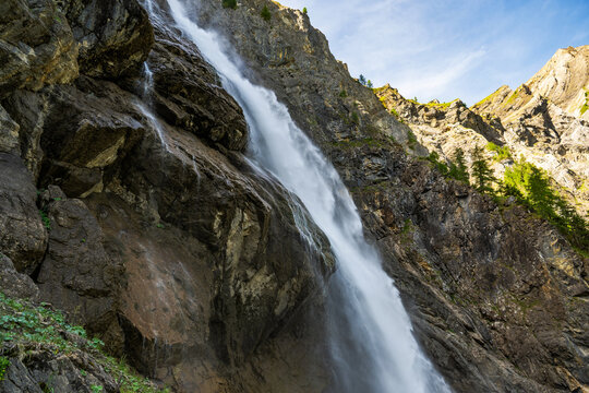 Waterfall flows down rocky mountain during bright blue sky