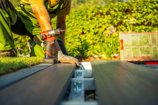 Worker builds wooden deck in garden during afternoon with drill in hand
