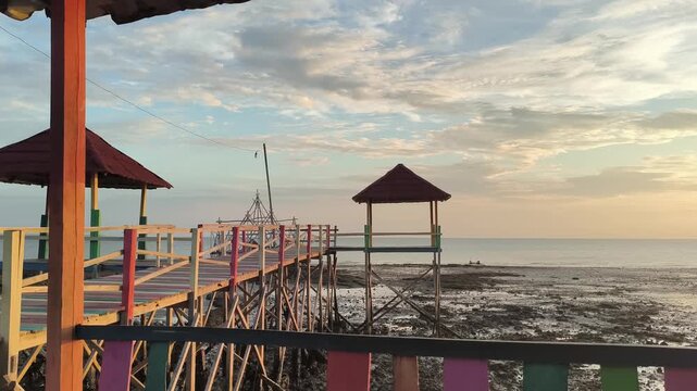 Colorful wooden walkway and gazebos on tropical beach at low tide during golden hour sunset