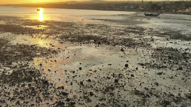 Golden sunset over tropical coastal beach at low tide with fishing boats and warm light