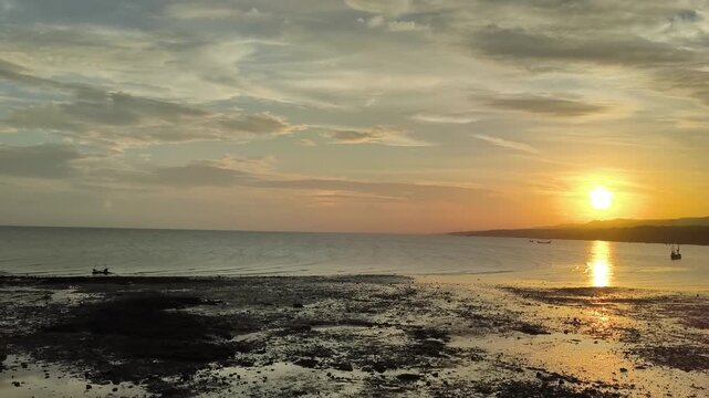 Golden sunset over tropical sea with clouds and reflection on coastal mudflat at low tide