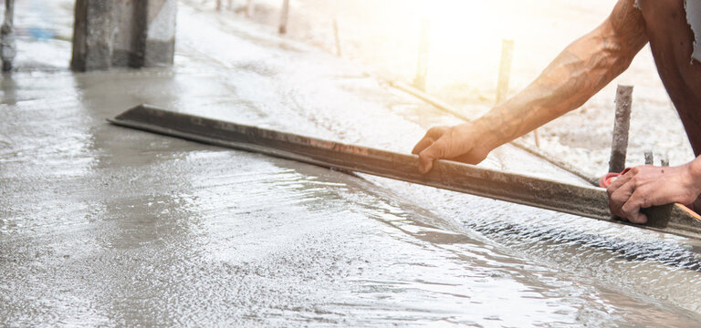 Close up of construction worker hands using an aluminum screed to level a new concrete floor. Professional masonry work and surface finishing for a building project or sidewalk repair.