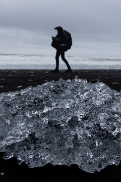 Glacial ice block on black sand with a person walking at Jokulsarlon Diamond Beach, Iceland