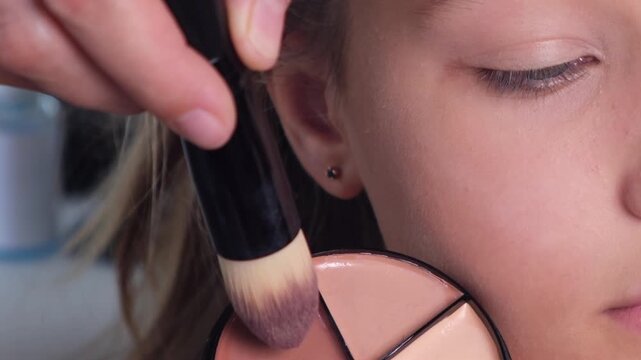 Close-up of a woman applying blush to her cheek with a soft makeup brush. Beauty routine, cosmetics, facial makeup and skincare concept