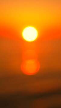 Radiant sun reflection shimmers on calm ocean waves during twilight. Vertical shot captures soft bokeh light patterns across the tranquil sea surface.