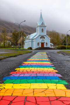 Blue Church Seydisfjardarkirkja behind a rainbow painted pavement street in Seydisfjordur, Iceland