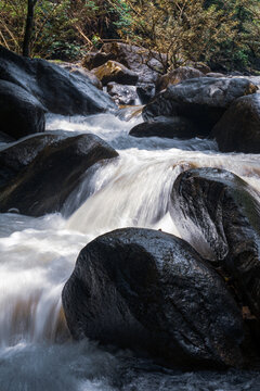 Close-up vertical shot of white water cascading through large dark river rocks.
