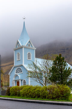 Blue Church Seydisfjardarkirkja behind green trees in Seydisfjordur, Iceland