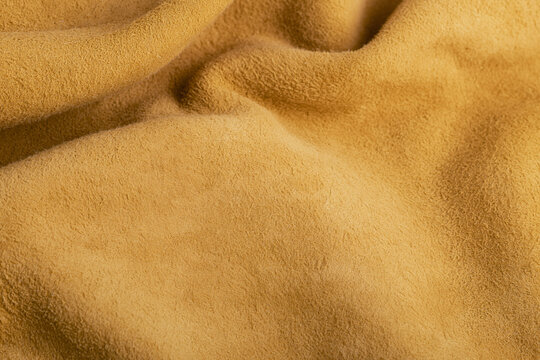 Abstract close-up of a draped natural brown suede leather fabric with soft folds and texture