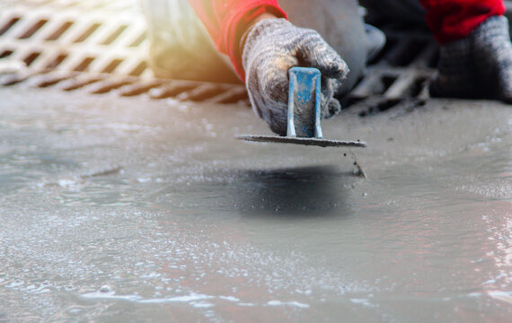 Mason hand in glove smoothing new concrete with a professional trowel tool. Skilled masonry worker performing surface finishing for pavement or sidewalk construction on site.