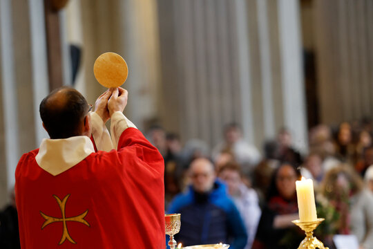 Saint-Jacques Collegiate Church.  A priest in a red chasuble raises the host during the celebration of Mass.  Eucharist. Elevation.