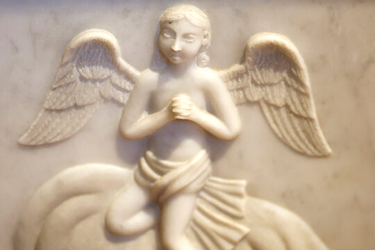 Saint-Jacques Collegiate Church.  A white marble bas-relief depicting a kneeling cherub with hands clasped; religious art.