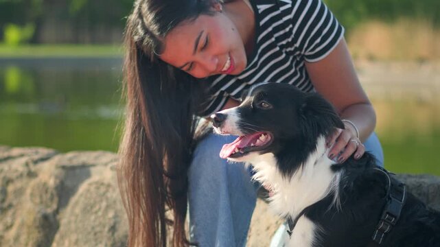 Happy young woman kissing her cute Border Collie dog by a scenic park lake during a sunny day
