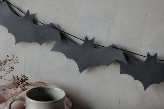 Paper bat cut-outs strung across a plain plaster wall, photo, desaturated grey-green and pale peach