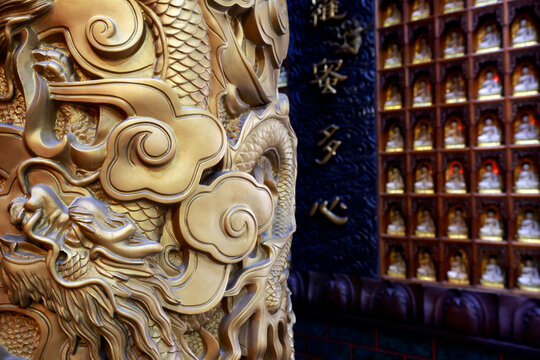 Van Phat Pagoda, or Temple of the 1,000 Buddhas. Detail of a gilded sculpture depicting a dragon and clouds. A row of small Buddha statues can be seen in the background. Ho Chi Minh City, Vietnam.