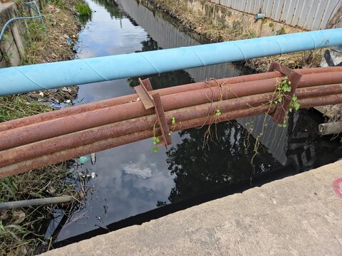 Rusty and Blue Industrial Pipes Crossing Over a Drainage Canal