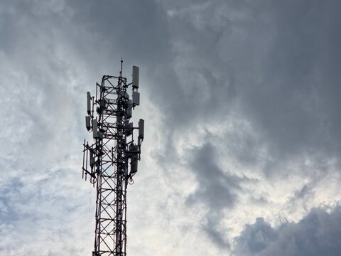A telecommunications cell tower equipped with various antennas against a dramatic, cloudy sky.