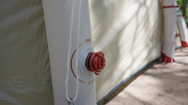 A macro view of a red pressure valve on a white inflatable tent support beam shows 7 PSI markings. Concept of modern camping technology, durable outdoor gear, and inflatable structure design