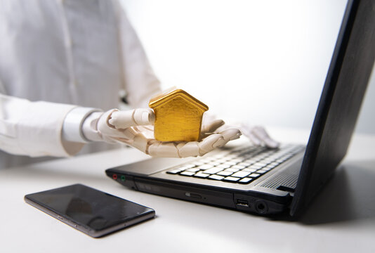 Robot Hand Holding Small Golden House Model near Laptop for Smart Home Concept