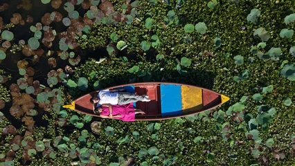Fotobehang Lotusbloem Aerial drone view of a couple enjoying a colorful boat ride across a scenic lake covered with lotus leaves and aquatic plants, surrounded by lush greenery.  © Vishal