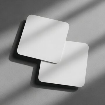 Two Blank Square Coasters Overlapping on a Soft Textured Grey Background Surface