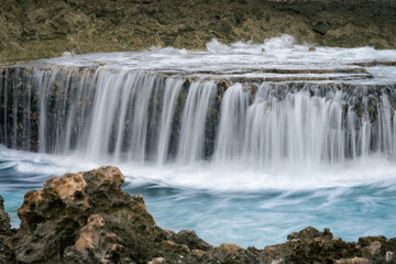 Ocean cascade spilling over limestone shelf with turquoise water © Nils
