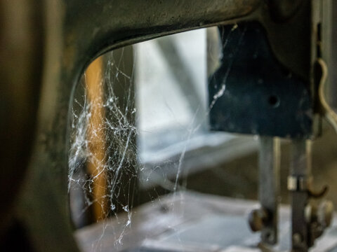 Detailed view of thick cobwebs spun inside the cast iron frame of an antique sewing machine