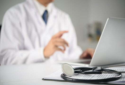 medical records clipboard stethoscope desk focus blurred doctor typing laptop background clinic working healthcare professional patient information diagnostic report health insurance consultation