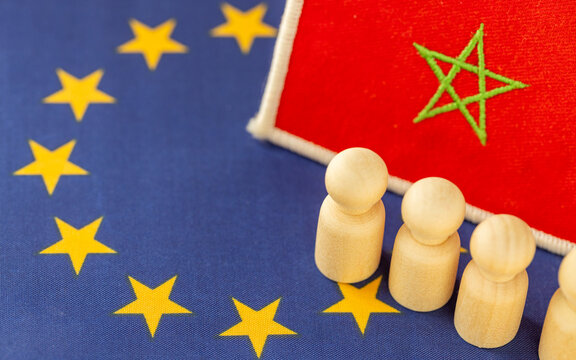 Morocco flag patch and wooden figures on the European Union flag background. Economic migration crisis, African refugees, international relations and EU external border.