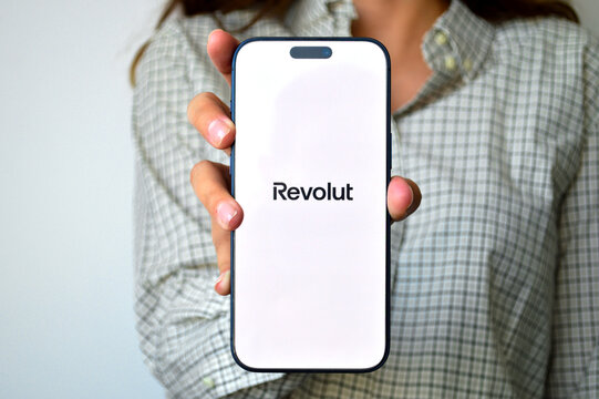Woman holding modern smartphone displaying a digital banking fintech application logo on bright white screen toward the camera