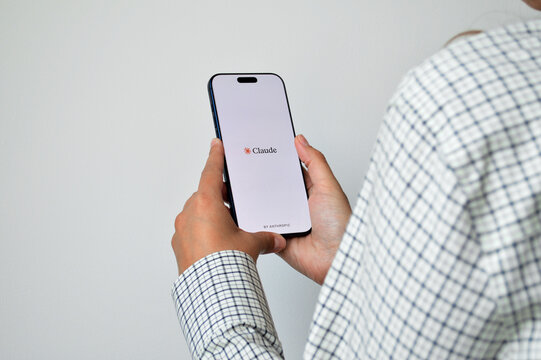 Person holding modern smartphone displaying Claude AI application splash screen by Anthropic against clean white background