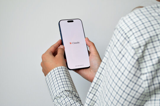 Person holding a modern smartphone displaying an AI assistant application splash screen, wearing a white plaid shirt against a neutral light gray background