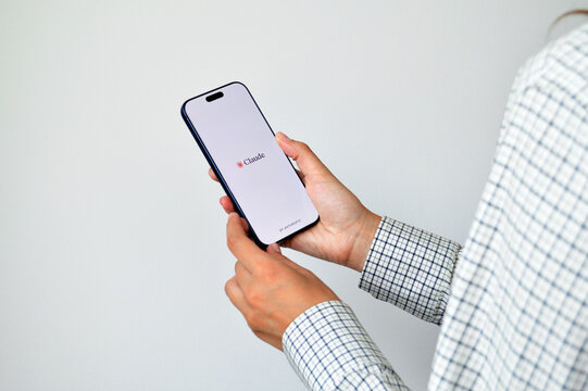 Person holding modern smartphone displaying Claude AI application splash screen on bright white background in casual business setting