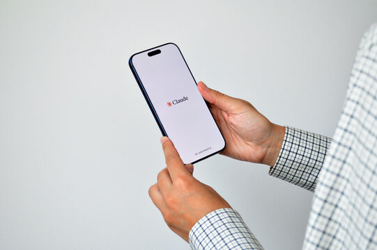 Hands of a professional person holding an iPhone displaying the Claude AI app splash screen by Anthropic against a clean white background