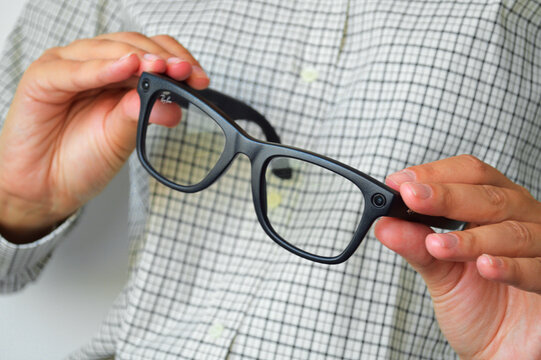 Person holding modern black smart glasses with embedded camera and wayfarer style frames, showcasing wearable technology innovation and connectivity