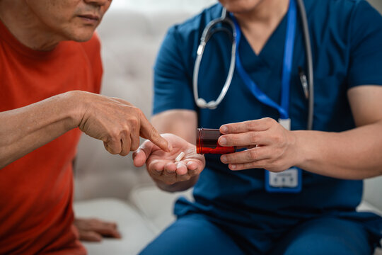 Caregiver Support for Senior Medication Management as a Male Healthcare Worker in Blue Medical Scrubs Reviews Medicine with an Asian Elderly Man at Home