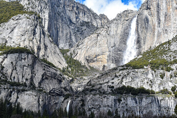 Bridalveil Fall cascades down towering granite cliffs in Yosemite National Park, California. Fresh snowfall blankets the surrounding Sierra Nevada peaks beneath dramatic blue skies and towering clouds © Gerard