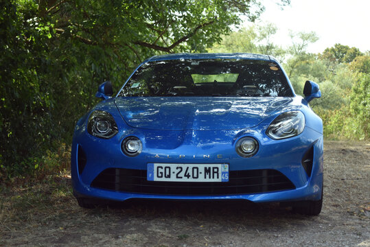 St- Amand Montrond - France - 2 August 2026 - Front view of a blue Alpine A110 sports car parked at the edge of a forest, showing a modern performance vehicle in a natural outdoor setting.
