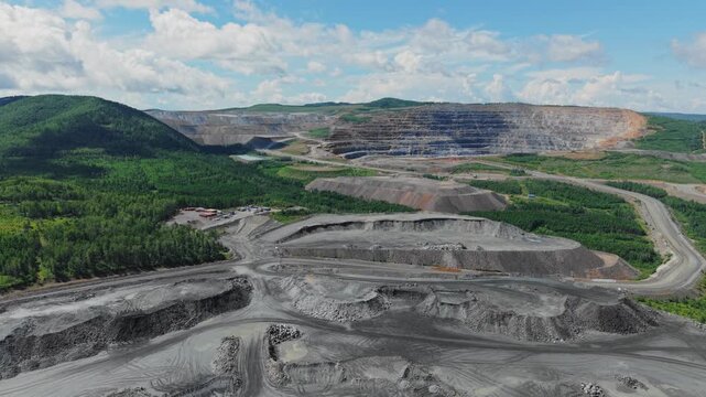 Aerial view of big open pit mine with heavy machinery and haul trucks on winding road in quarry gold, copper and iron ore.
