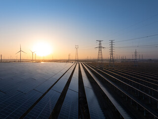 Solar power plant and wind turbines at sunrise with orderly photovoltaic panels and transmission...