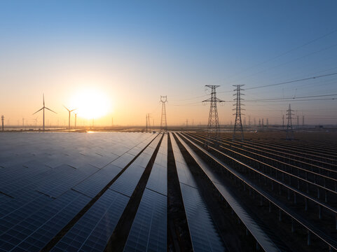 Solar power plant and wind turbines at sunrise with orderly photovoltaic panels and transmission towers
