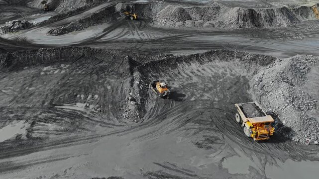 Aerial view of large dump truck hauling copper, gold ore across open quarry pit with loader and tire tracks.