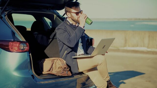 Businessman Working On Laptop Sitting In Car Trunk Open. Remote Work. Outdoor Office