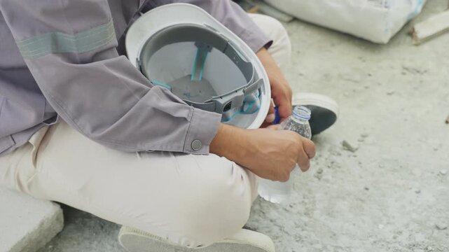 Person sitting home inspector helmet water bottle concrete site inspection calm break worker holding hard hat outdoor safety scene tired construction job site breaks