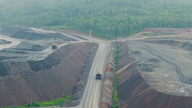 Aerial view of mining truck driving along haul road through open pit mine with spoil heaps.