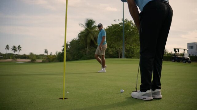 Golfer successfully putting a golf ball into the hole while his friend watches and celebrates