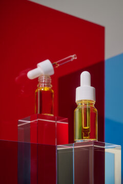 Two dropper bottles with golden liquid on geometric pedestals