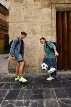 Two young men play soccer in a city street during the day