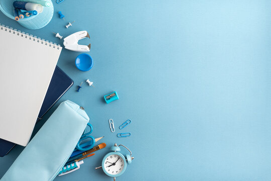 A flat lay of school and art supplies on a blue background with a notebook pencil case and alarm clock