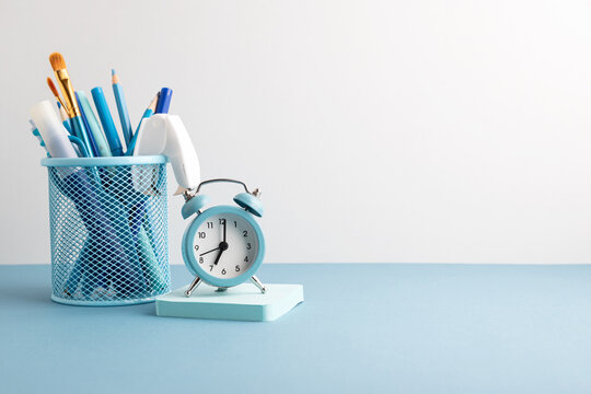 Blue desk organizer with pens and pencils and a retro alarm clock